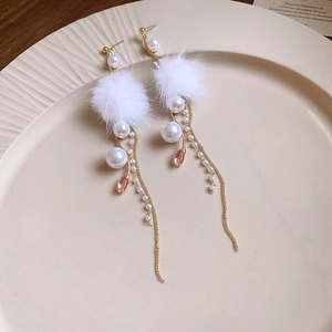 Detail of elegant gold earrings with white pompom, pearls and pink crystal pendant