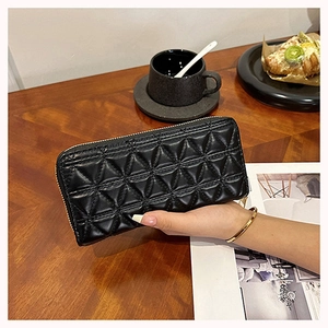 Detail showing hand holding black quilted long wallet over a cafe table background