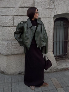 Detail of elegant dark green glossy faux leather jacket with high-neck black dress