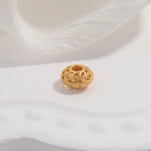 Macro shot of a hollow gold filigree spacer bead with intricate floral metalwork details