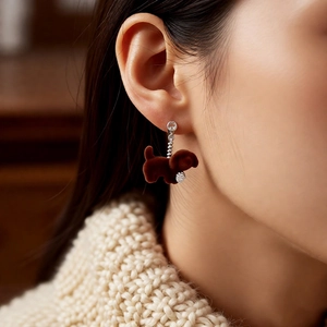 Close-up of a brown flocked puppy drop earring with zircon on a model wearing knitwear