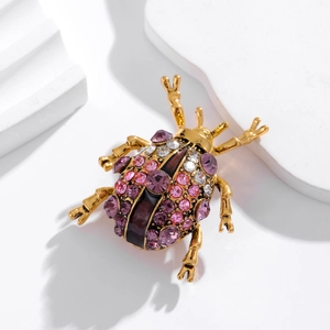 Broche scarabée dorée ornée de strass violets et transparents sur fond blanc
