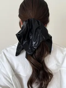 Detail of a large silver faux leather scrunchie with metallic shine on a high ponytail