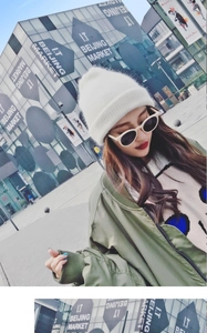 Close-up of a white knit beanie paired with a green bomber jacket and trendy sunglasses