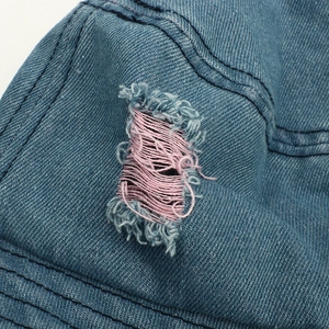 Detailed close-up of blue distressed denim fabric with raw edges and pink thread contrast