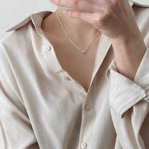 Close-up of minimalist silver necklace with rectangular clear stone on a satin shirt
