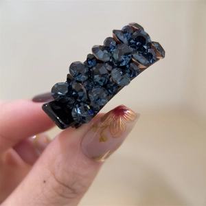 Gros plan d'une petite barrette en strass bleu marine tenue par une main avec nail art