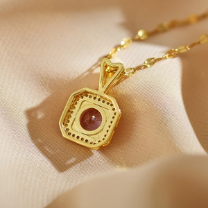 Macro shot of gold square pendant featuring a peach-orange gem on a fine link chain