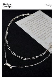 Detail of silver layered double chain necklace with cylindrical spring pendant on black fabric