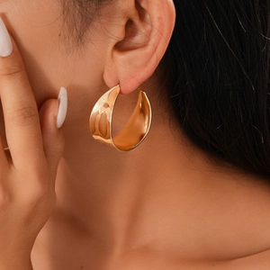 Close-up of elegant gold C-shaped chunky hoop earrings worn by a model in soft light