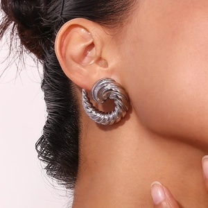 Silver twisted metal earrings with geometric swirl texture on female model's ear