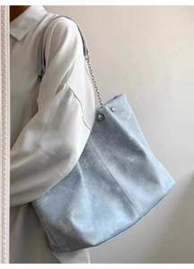 Detail of light blue denim tote bag with silver chain strap shown on person