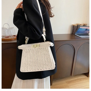 Detail of white woven texture handbag featuring a gold turn-lock closure and leather strap
