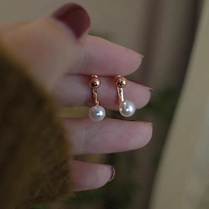 Detailed view of rose gold freshwater pearl drop earrings held by hand for size reference