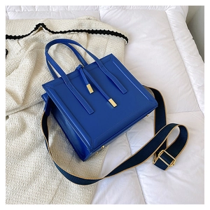 Detail of royal blue leather crossbody bag showing golden hardware and wide fabric strap