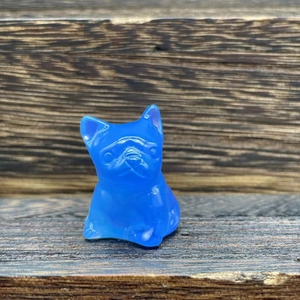 Macro detail of blue translucent crystal French Bulldog figurine on dark wood surface