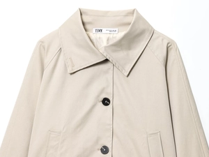 Dettaglio del trench beige con bottoni neri ed etichetta del marchio sul collo
