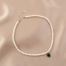 Detail of freshwater pearl necklace with black heart pendant on silk background