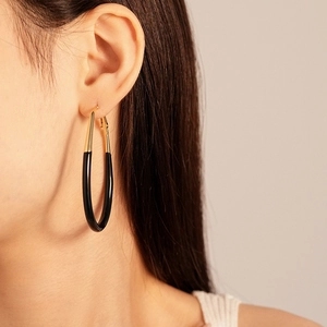 Close-up of a large oval hoop earring with gold metal and black enamel finish on model