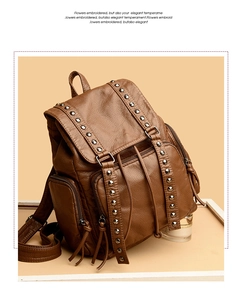 Detail of dark brown leather backpack featuring silver studs and long fringe zipper pulls