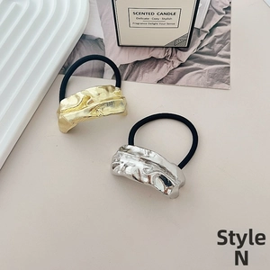 Detail of gold and silver irregular metal plates on black elastic hair ties on a tray