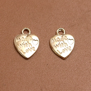Primer plano de colgantes de corazón dorados grabados Made with Love para joyería DIY