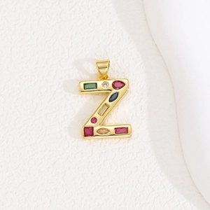 Detail of a gold letter Z pendant featuring colorful zircon stones on a white background