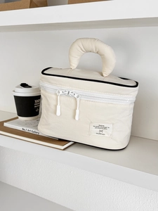 Detailed view of a cream nylon makeup bag with black piping on a minimalist shelf