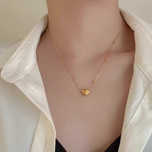 Detail of a heart pendant necklace with small bead accents on a gold-plated chain