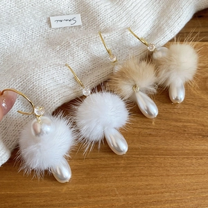 Detail of C-shaped winter earrings with soft fur balls and teardrop pearl pendants