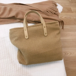Handcrafted jute tote bag with creamy white leather handles on a minimalist bed setting