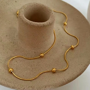 Detail of 18K gold snake bone chain with small metal beads on ceramic display stand