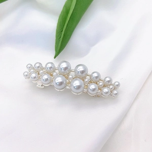 Detailed view of pearls on silver hairpin against white silk and green leaf