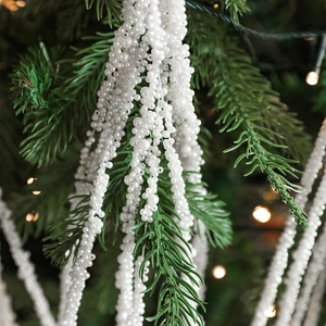 White pearl bead spray decoration on green Christmas tree branch with warm lights