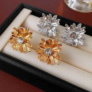 Detailed macro view of gold and silver flower stud earrings with crystals in a box