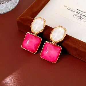 Details von eleganten Goldohrringen mit weißen und rosa Steinen auf braunem Leder