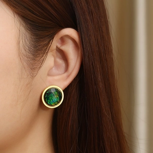 Detail of a vintage golden round earring with shimmering green and blue resin inlay
