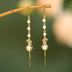 Detailed close-up of golden long tassel earrings with pearls and opal beads on a metal stand