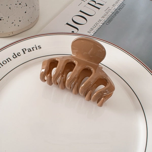 Glossy light brown hair claw clip on ceramic plate with elegant aesthetic background