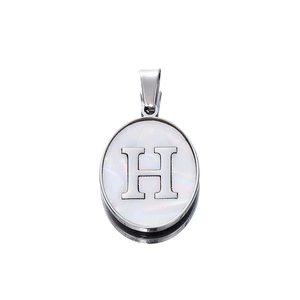 Macro shot of oval stainless steel pendant with white shell inlay and letter H detail