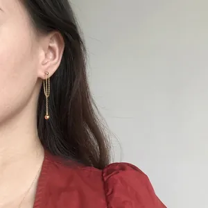 Elegant gold chain tassel earrings with sphere pendant shown on a model with a red V-neck