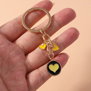 Close-up of golden keychain with black enamel round pendant and yellow heart charms