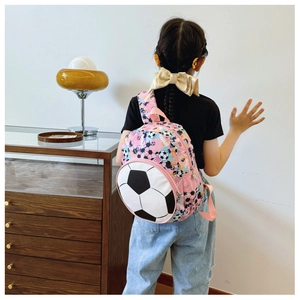 Pink kids soccer backpack worn by a girl in a home setting with 3D football pocket