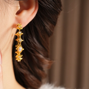 Close-up of vintage gold hoop earring with star detail and pearl on female model