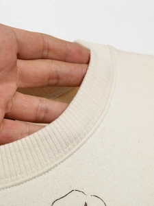 Close-up of the ribbed crew neck collar on a beige cotton sweatshirt showing knit texture
