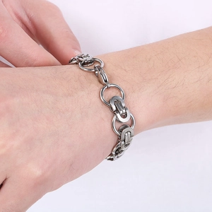 Close-up of men's silver stainless steel Cuban link bracelet with large rings on wrist