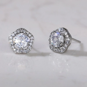 Macro shot of silver flower earrings with pavé zircons reflecting on white marble