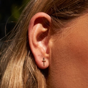 Close-up of gold sword-shaped earring with black accents worn on a model's earlobe