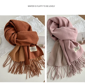 Detail of soft winter scarves with long fringe and white brand label in caramel and pink
