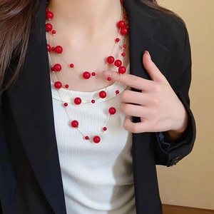 Detail of multi-layer gold chain necklace with vibrant red round beads on a model